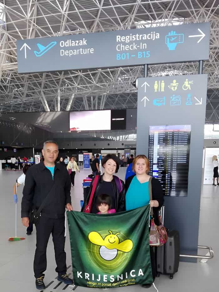 Obitelj u zračnoj luci s transparentom "Krijesnica".
